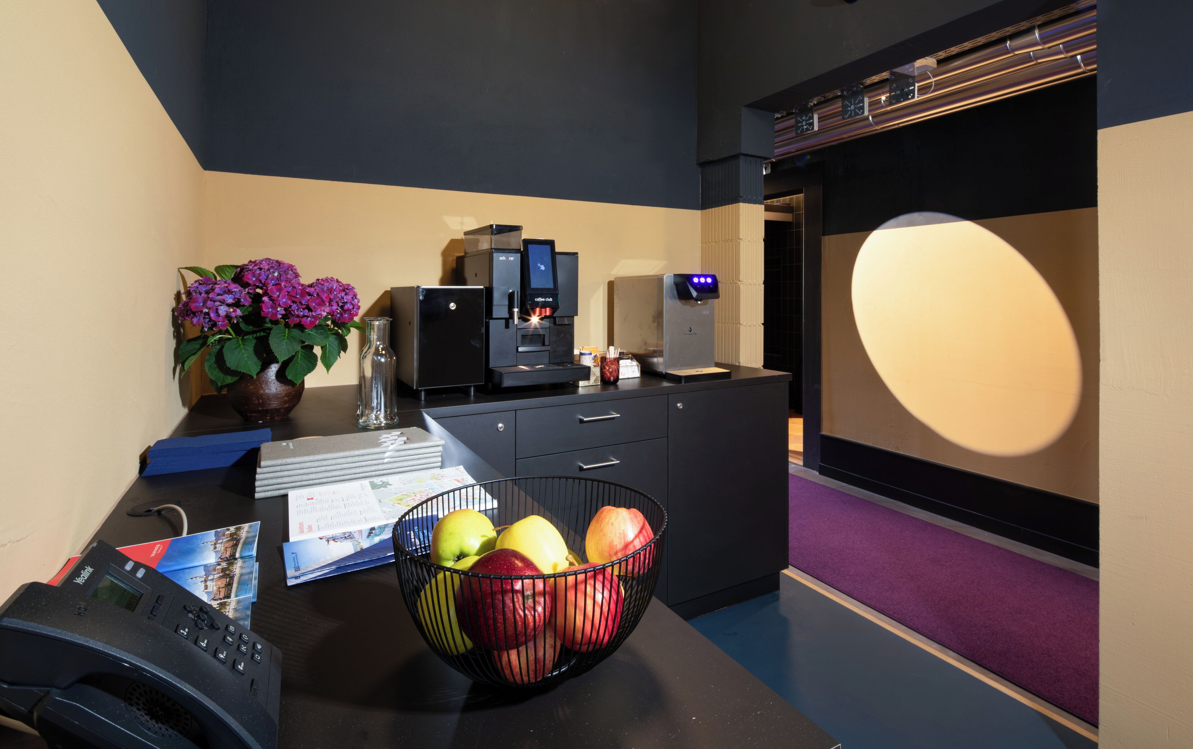A modern kitchen with a coffee machine, a bowl of fruit, and a vase of flowers on the counter.