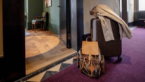 Et værelse med fiskebensparketgulv, et lilla tæppe, en Louis Vuitton kuffert, en brun håndtaske og en stol.