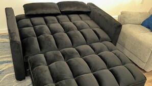 A black sofa with a tufted design, positioned in a room with a blue rug and a grey armchair.