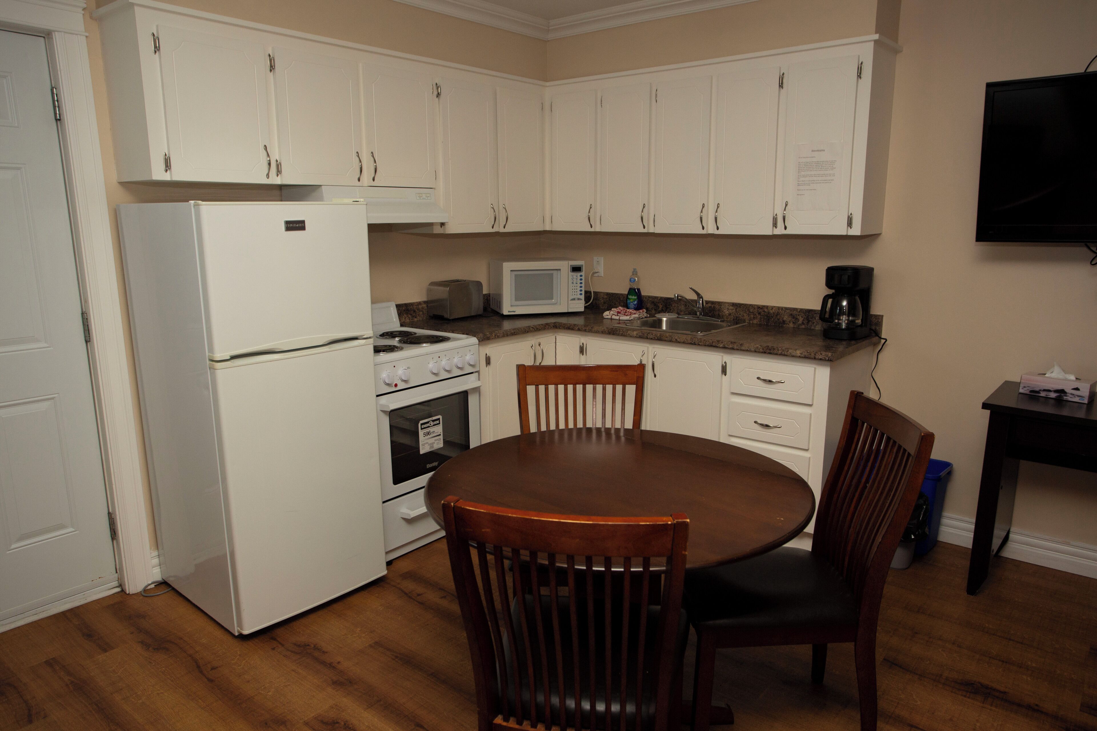 A compact kitchen with white cabinets, a stove, a microwave, and a dining table with chairs.