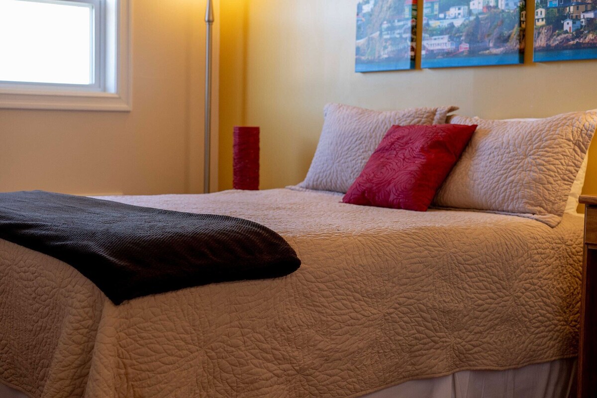 A neatly made bed with a quilted cover, a red pillow, and a black throw blanket.