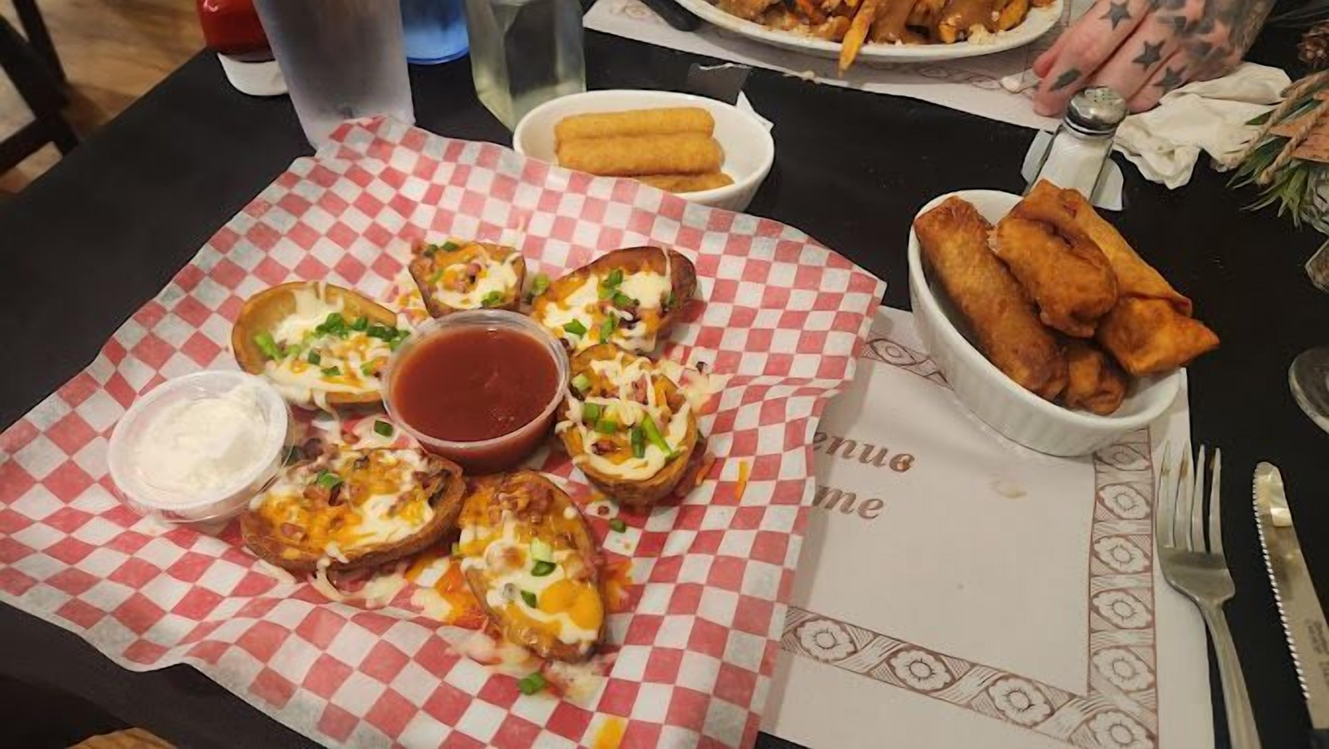 Une table avec différents plats, notamment des pommes de terre au four garnies de fromage et d’oignons verts, un bol de sauce pour tremper, et un récipient de sauce ranch.