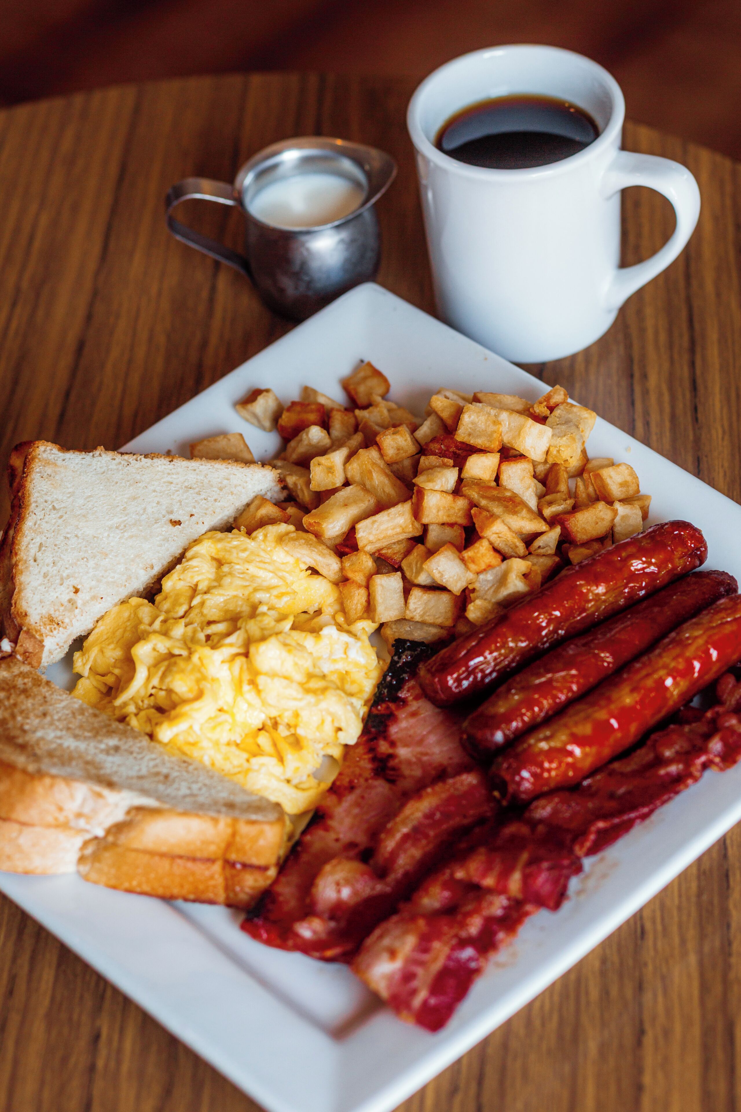A breakfast plate with toast, scrambled eggs, bacon, and hash browns.