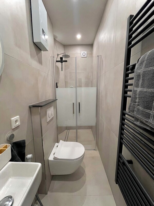 A compact bathroom with a white toilet, a glass-enclosed shower, and a towel rack.