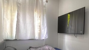 A bedroom with a bed, curtains, a TV mounted on the wall, and a window. - Small and fine city apartment in Saarbrücken (Saarbrücken)