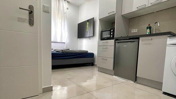 A modern kitchen with a microwave, dishwasher, and sink. There is a bed with a blue mattress in the background. - Small and fine city apartment in Saarbrücken (Saarbrücken)