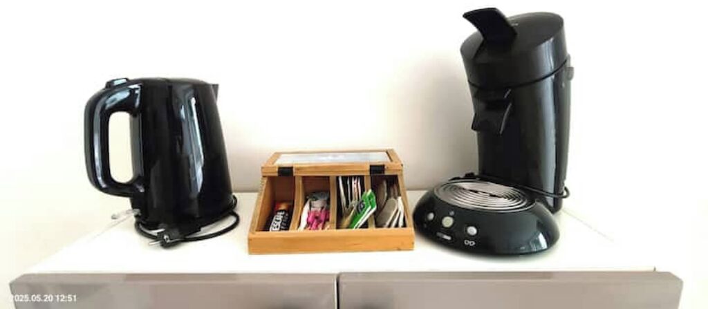 Una cocina con cafetera, hervidor y una caja de madera con utensilios.