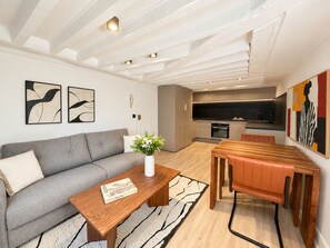 A modern living room with a sofa, coffee table, and a dining area with a table and chairs. - 1533 Petites écuries (Paris)
