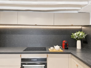 A modern kitchen with a black countertop, a built-in oven, and a coffee maker on the counter. - 1533 Petites écuries (Paris)