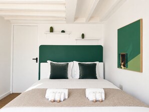 Een net opgemaakt bed met witte lakens en twee verzorgingsproducten van Nuxe op het bed.