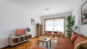 Un salon comprenant un canapé, un téléviseur, une table basse et un coin repas avec des chaises et une table.