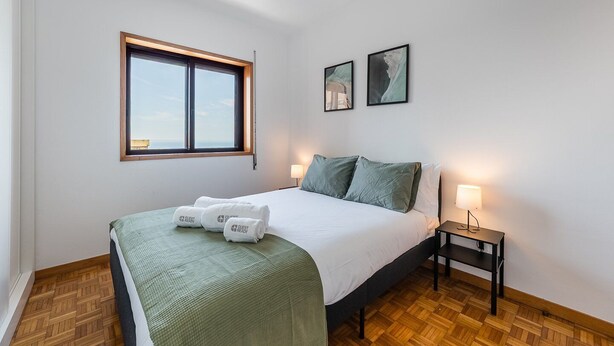 Une chambre d’hôtel avec un lit, une table de chevet, une fenêtre et deux tableaux encadrés au mur.