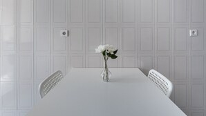 Une table à manger blanche, ornée d’un vase de fleurs blanches au centre, et flanquée de deux chaises blanches.