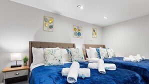 Una habitación de hotel moderna con dos camas, una mesita de noche con lámpara y obras de arte en las paredes.