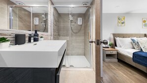 Un baño moderno con cabina de ducha de vidrio, tocador blanco y cama con manta azul.