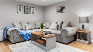 Una sala moderna con un sofá gris, una mesita de centro con libros y una mesita auxiliar con una lámpara.