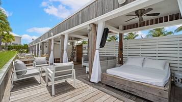 A wooden deck with a bed, chairs, and a ceiling fan.
