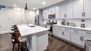 Una cocina moderna con gabinetes grises, electrodomésticos de acero inoxidable y una isla central con taburetes.