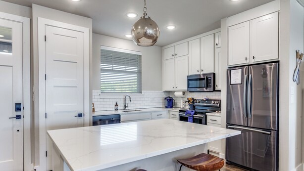 A modern kitchen with white cabinetry, a large island with stools, stainless steel appliances, and recessed ceiling lighting. - Oasis Luxury Lakefront Condo:1st Floor, Pool, HotTub, Dining, Boating, Fishing! (Graford)