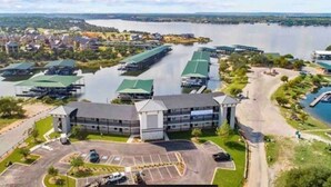 An aerial view of a hotel with multiple buildings, a parking lot, and a body of water in the background. - Oasis Luxury Lakefront Condo:1st Floor, Pool, HotTub, Dining, Boating, Fishing! (Graford)