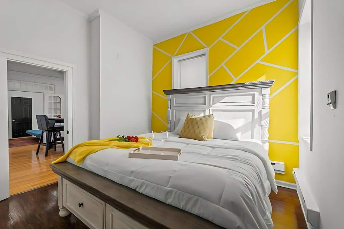 A bedroom with a bed, a bedside table, a chair, and a desk. There is a window with a view of the outside.