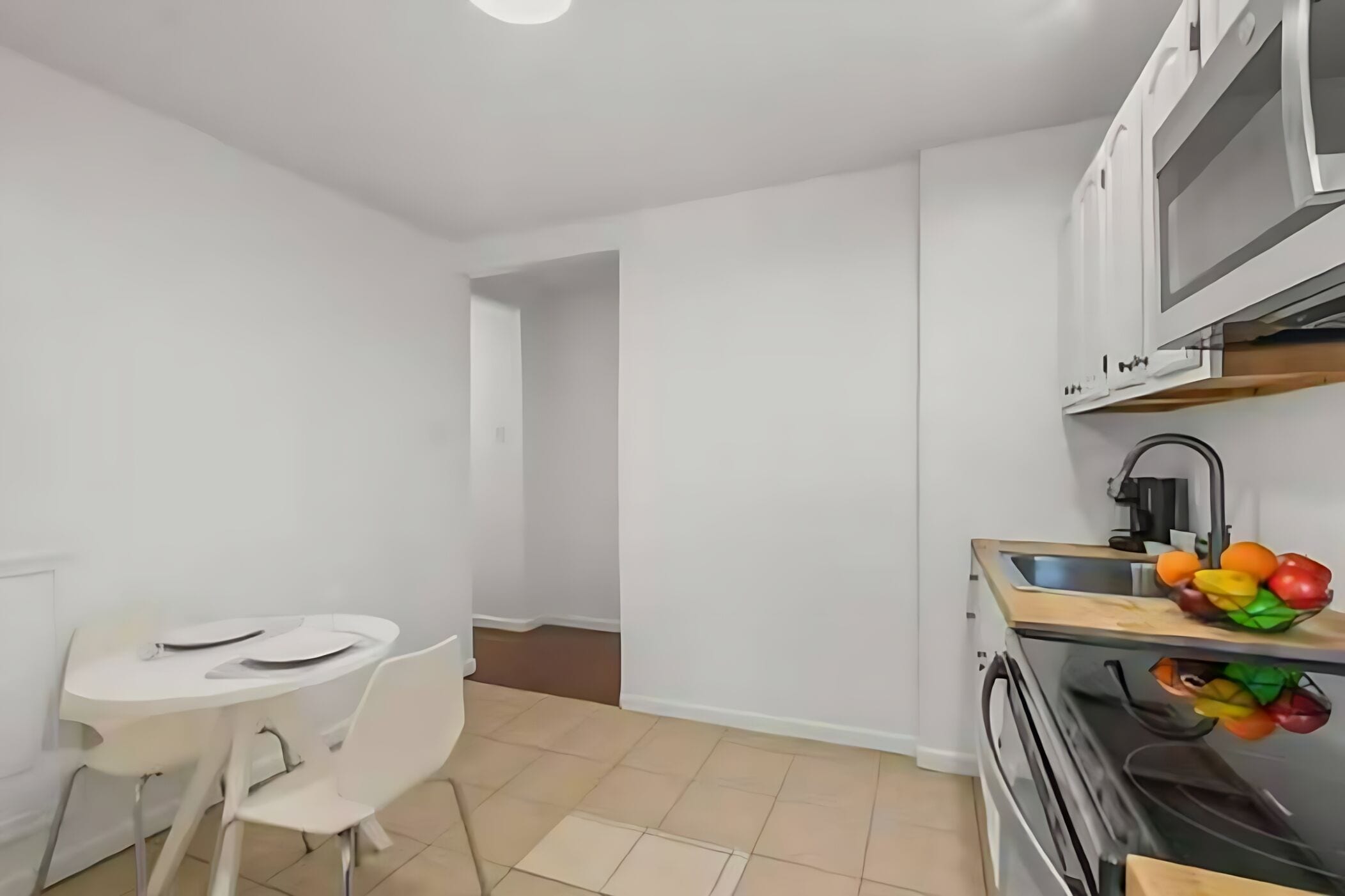 A small, modern kitchen with white cabinets, a sink, and a countertop with fruit.