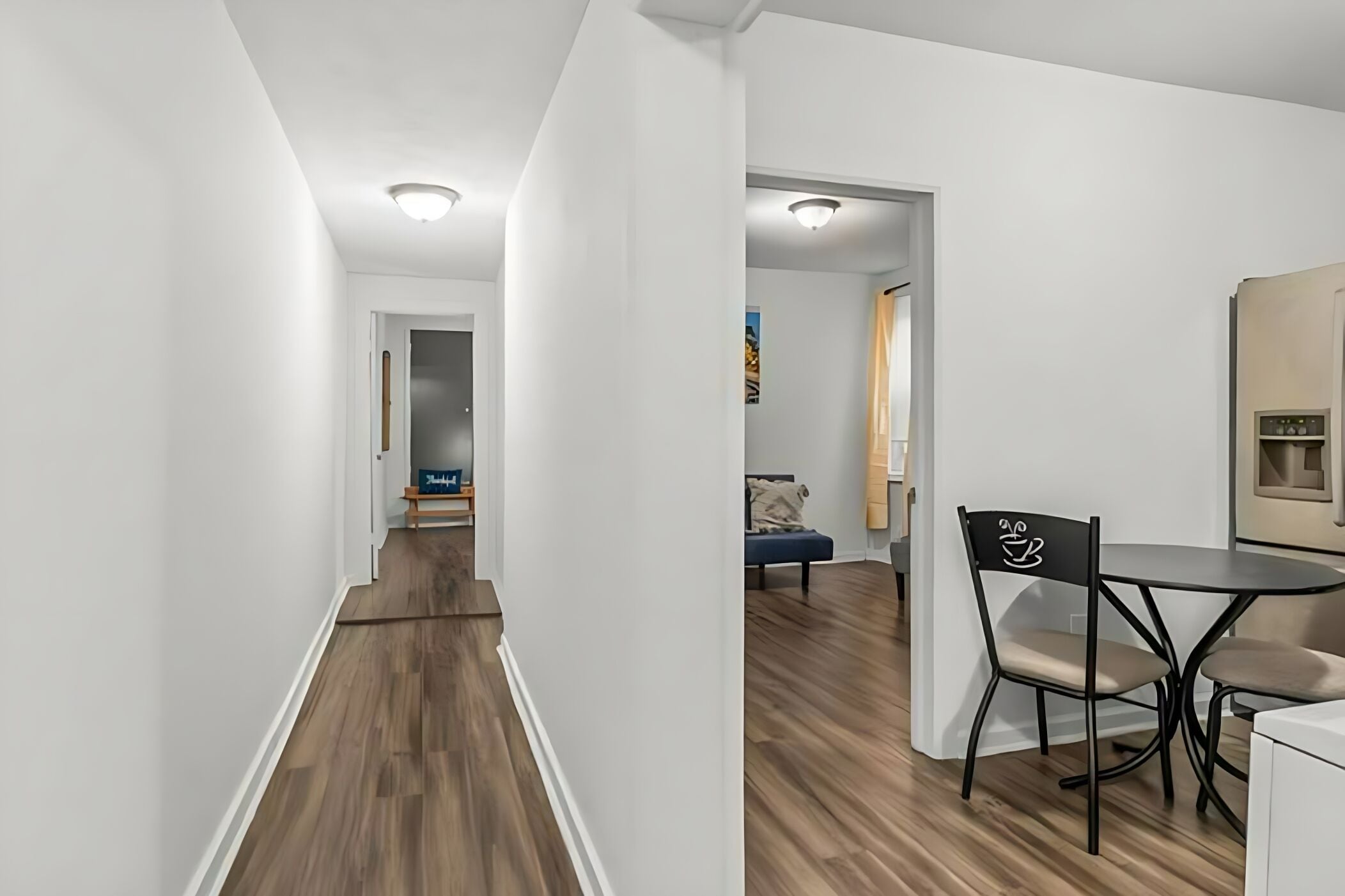 A modern interior with a wooden floor, white walls, a dining area with a table and chairs, and a visible kitchen area.