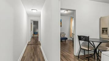A modern interior with a wooden floor, white walls, a dining area with a table and chairs, and a visible kitchen area.