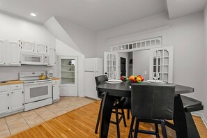 A modern kitchen with white cabinetry, a built-in microwave, and a dining area with a black table and chairs. - West Philly Suites (Philadelphia)