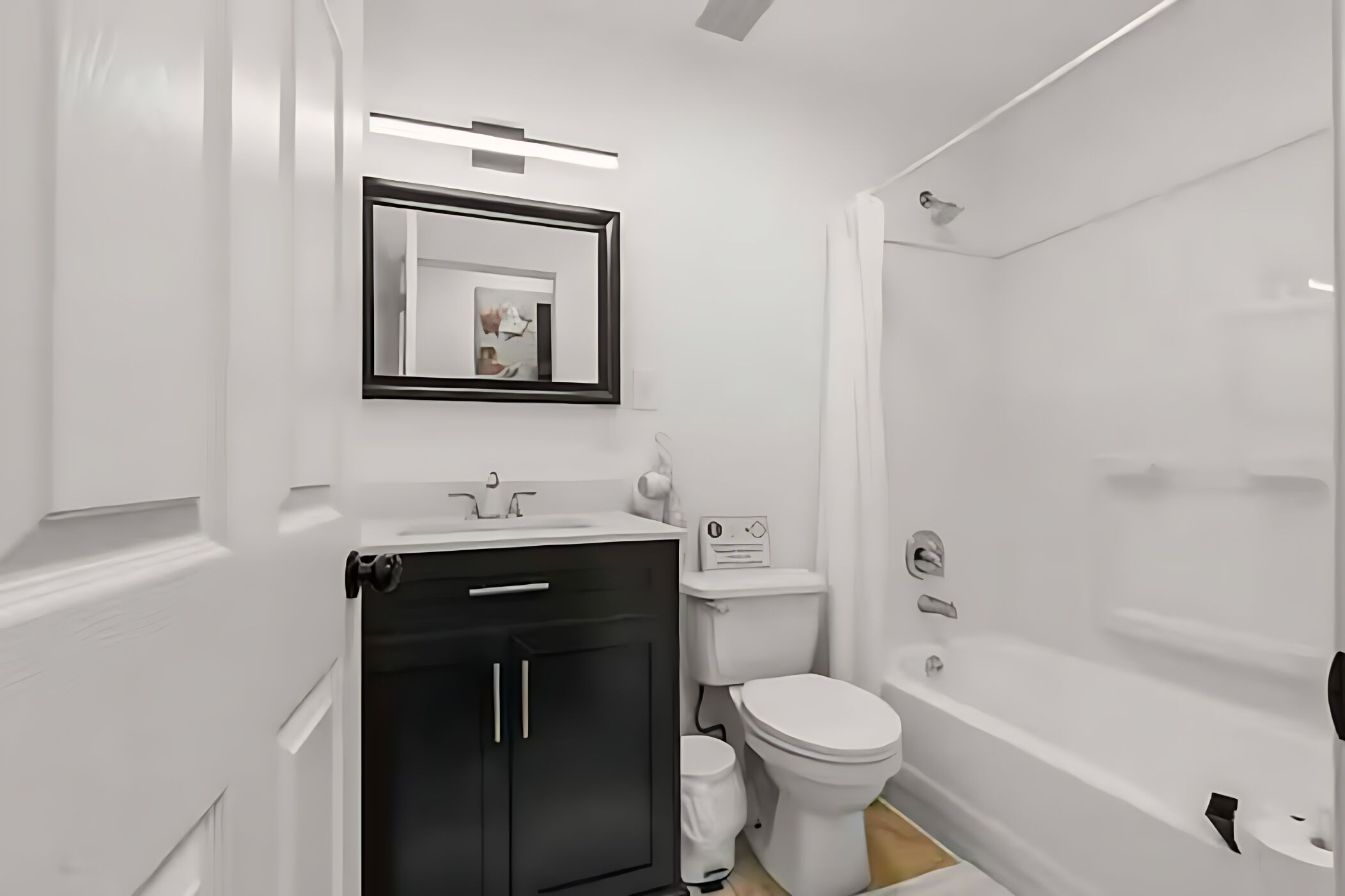 Un baño moderno con lavamanos blanco, mueble negro, inodoro y bañera.
