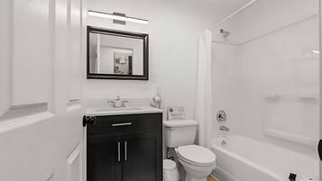 Un baño moderno con lavamanos blanco, mueble negro, inodoro y bañera.
