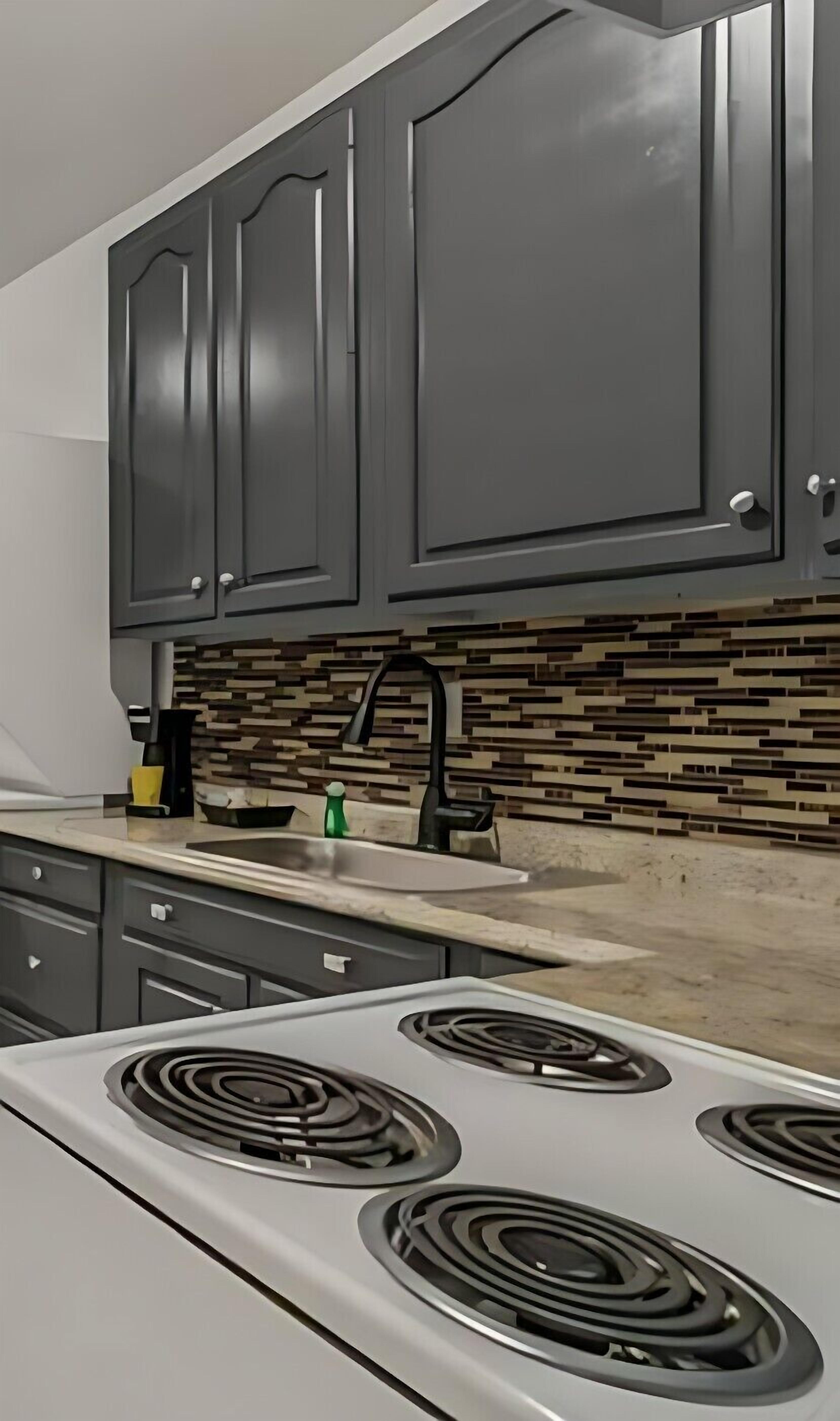 A kitchen with dark cabinets, a tiled backsplash, and a white stove with four burners.