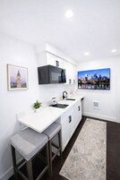 Una cocina moderna con muebles blancos, un microondas integrado, un lavamanos y un cuadro de un paisaje urbano en la pared.