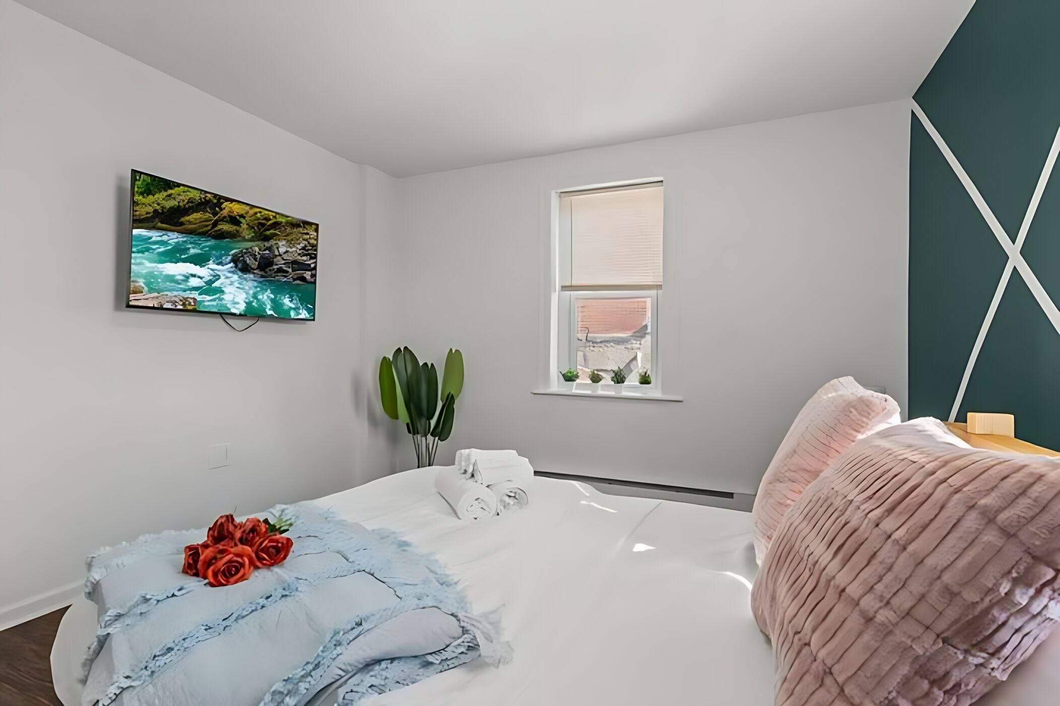 A bedroom with a bed, a painting of a river, a window with blinds, and a green wall.