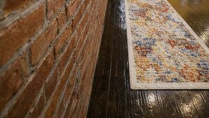 Un pasillo con pared de ladrillo, alfombra estampada y escalera con barandilla.