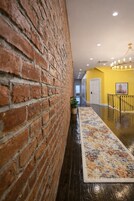 Un pasillo con pared de ladrillo, alfombra estampada y escalera con barandilla.
