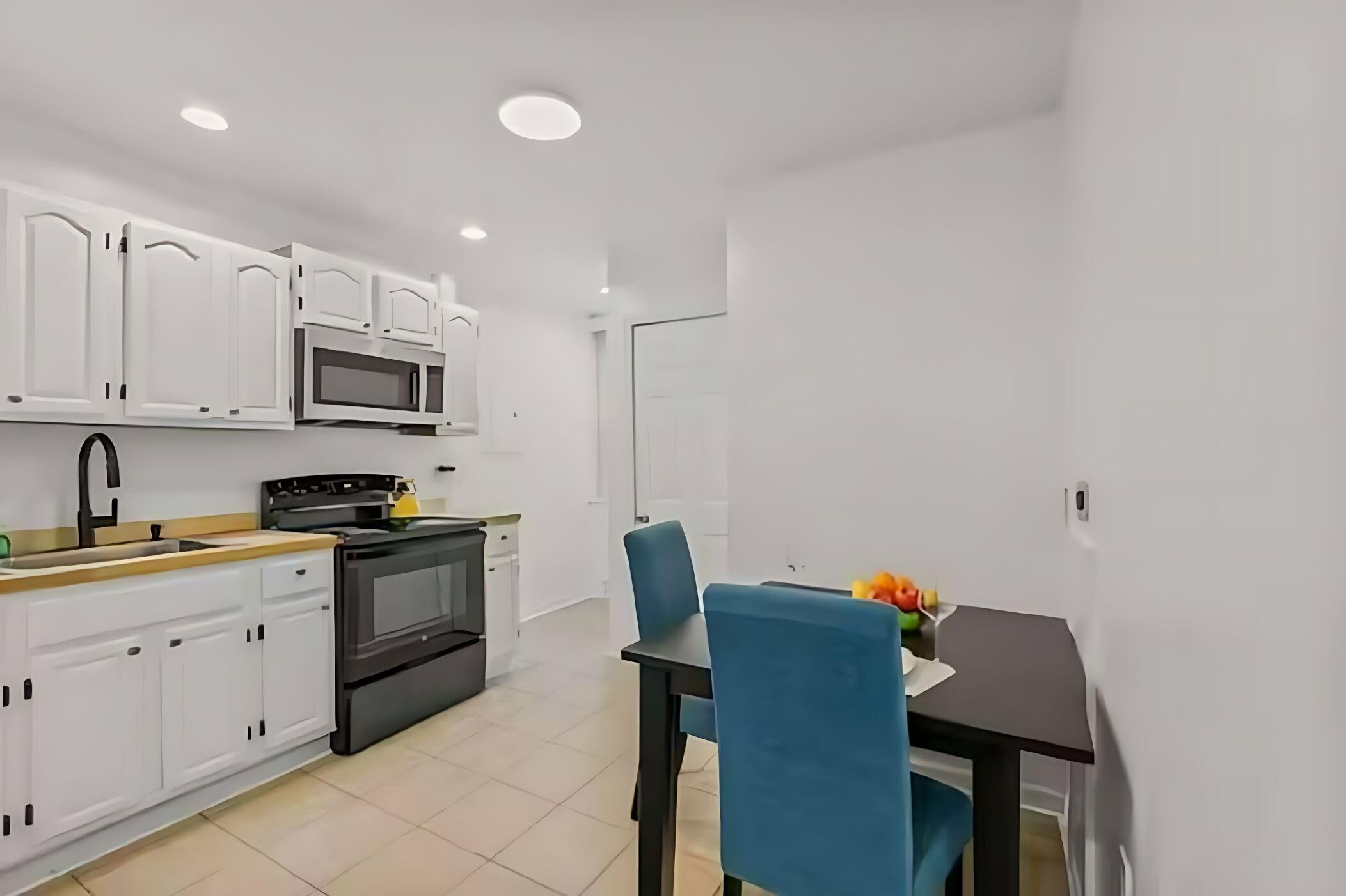 A modern kitchen with white cabinets, a microwave, stove, and a dining area with blue chairs and a table.