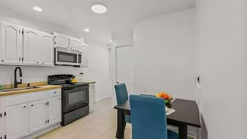 A modern kitchen with white cabinets, a microwave, stove, and a dining area with blue chairs and a table.