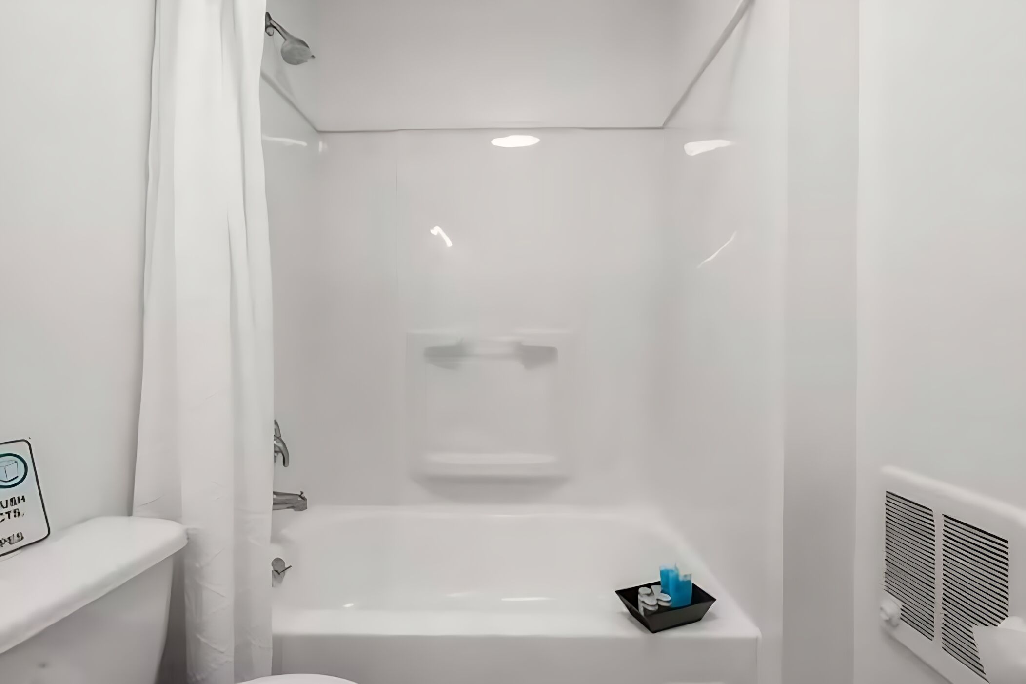 A white bathroom with a bathtub, a shower, and a toilet. There is a sign on the wall and a small tray with toiletries.