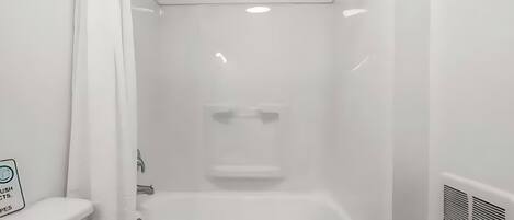 A white bathroom with a bathtub, a shower, and a toilet. There is a sign on the wall and a small tray with toiletries.
