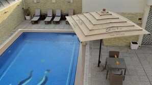 A swimming pool with lounge chairs and a covered seating area. - Premium Strato Hotel (Doha)