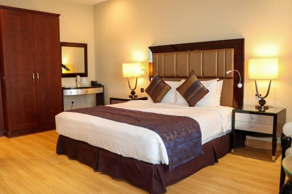 A hotel room with a large bed, two bedside tables with lamps, a wardrobe, and a mirror on the wall.