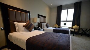 A hotel room with two beds, a small table, a chair, and a window with curtains. - Premium Strato Hotel (Doha)