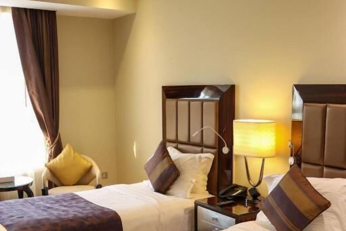 A hotel room with two beds, each with a headboard, a bedside table with a lamp, and a chair.