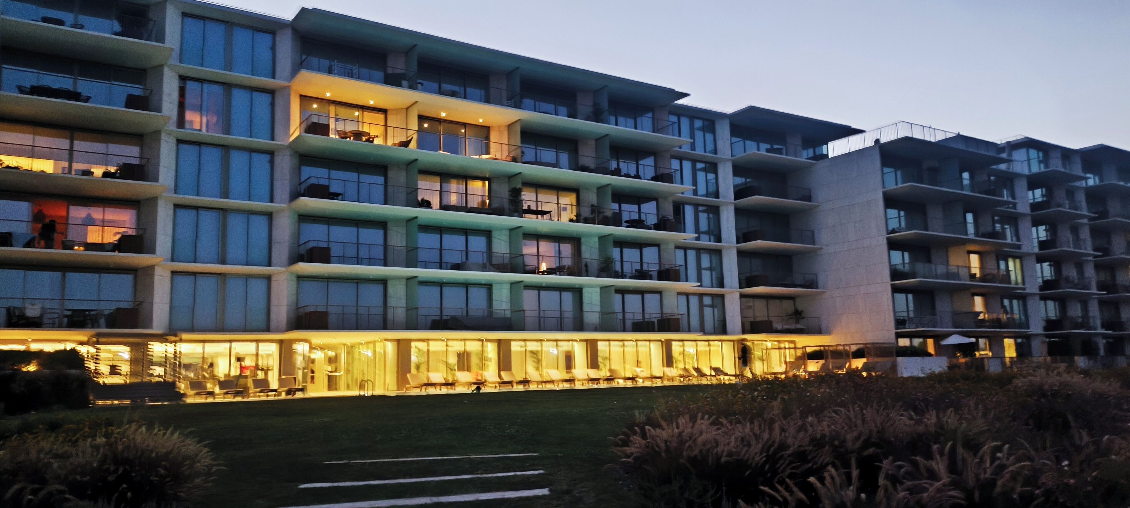 Un hotel de varios pisos con balcones, ventanas amplias y un área de entrada bien iluminada.