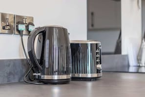 A kitchen with a kettle and a toaster on a countertop, connected to a power outlet.