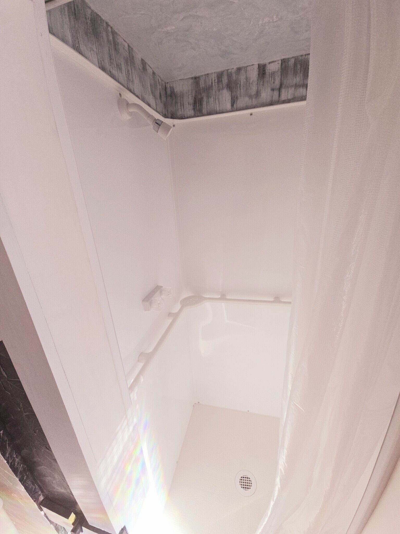 A corner of a room with a white shower enclosure and a wooden accent wall.