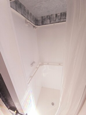 Rincón de una habitación con un box de ducha blanco y una pared de acento de madera.
