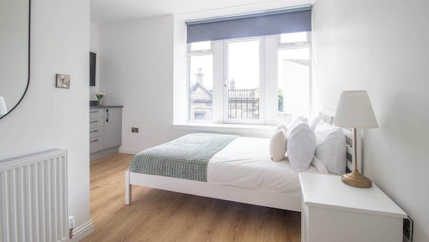 A bedroom with a bed, bedside table, lamp, window, and a view of buildings outside. - Double Ensuite Room + Shared Kitchen + Fast Wi-Fi (Grangemouth)