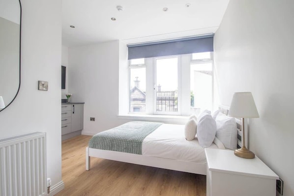 A bedroom with a bed, bedside table, lamp, window, and a view of buildings outside. - Double Ensuite Room + Shared Kitchen + Fast Wi-Fi (Grangemouth)